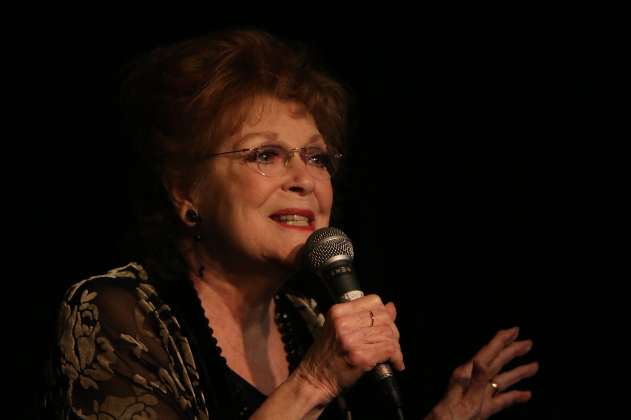 Woman singing into a microphone on stage.