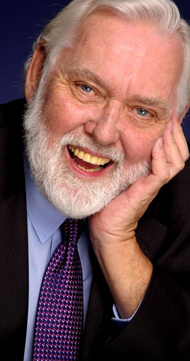 Smiling man with white beard and suit.